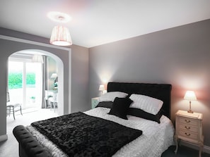 A bedroom with a bed, two bedside tables, a lamp, a window, and an arched doorway.