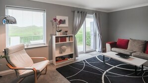 Ett modernt vardagsrum med en vit soffa, en vit fåtölj, en bokhylla och en svart matta.
