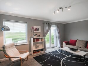 A modern living room with a white sofa, a white armchair, a bookshelf, and a black rug.