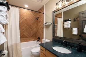 A bathroom with a herringbone wood floor, a bathtub, a toilet, a sink with a black countertop, and a mirror with a wooden frame. - Hidden Cabin Retreat with Private Deck & Firepit (Gainesville)