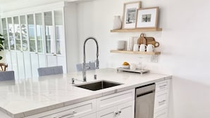A modern kitchen with white cabinetry, a marble countertop, a built-in dishwasher, and a window with a view of greenery.