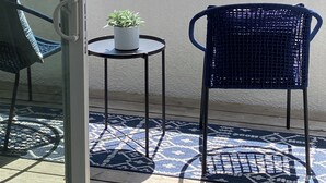 A balcony with two chairs, a small table with a plant, and a view of the ocean and buildings.