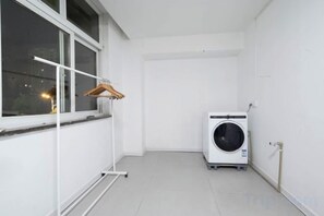 A laundry area with a washing machine, a drying rack, and a window with a view of the outside. - YIJING International Hotel (Fuyang)