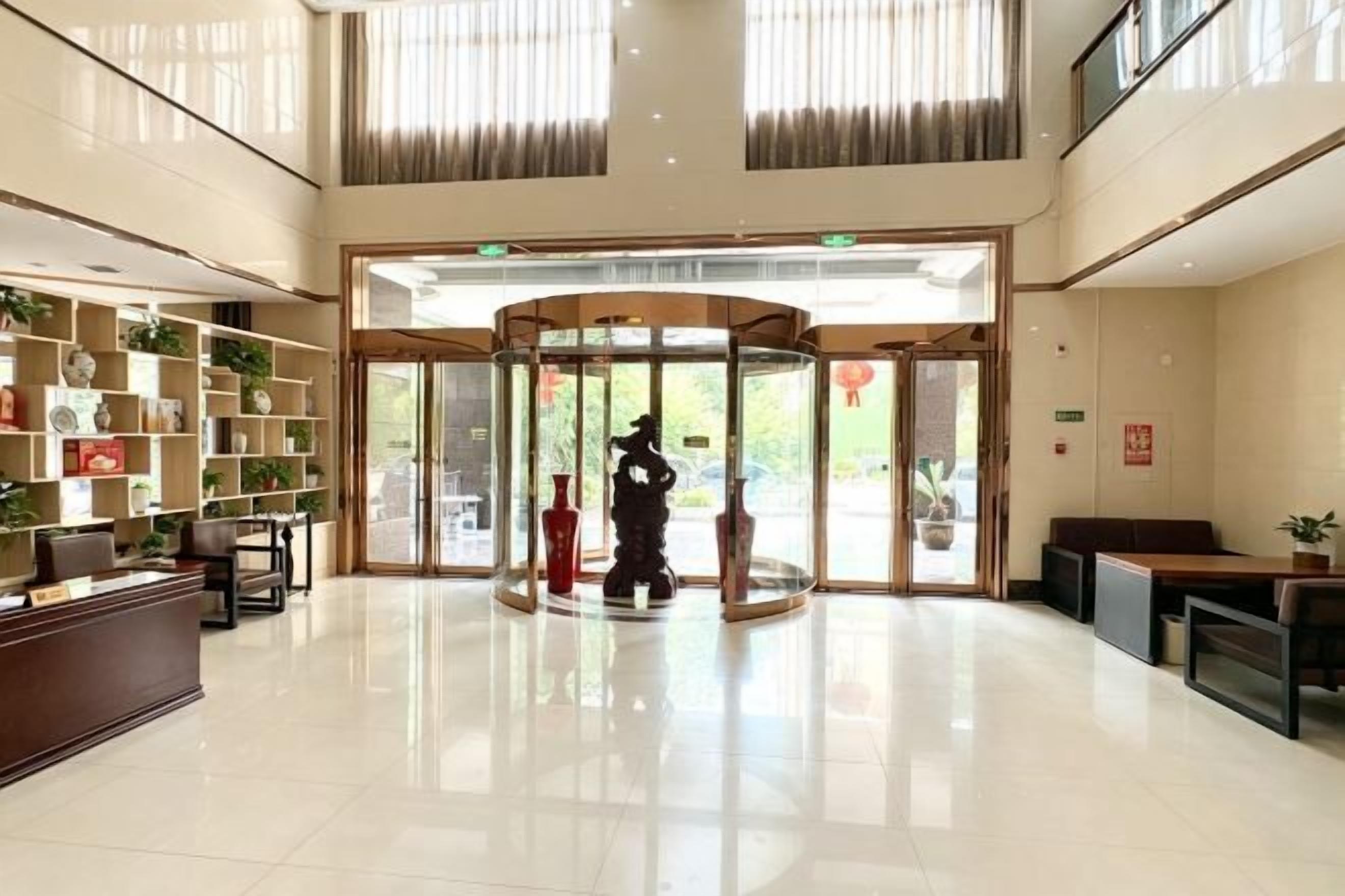 Un hall de hotel con mostrador de recepción, puerta giratoria y zona de estar con plantas en macetas.