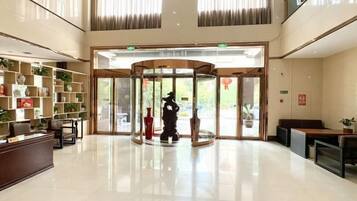 Un hall de hotel con mostrador de recepción, puerta giratoria y zona de estar con plantas en macetas.