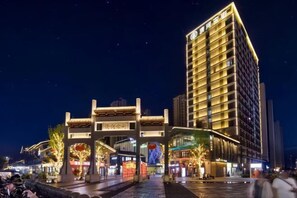Un hotel moderno con un arco de entrada tradicional, señalización iluminada y una fachada bien iluminada.