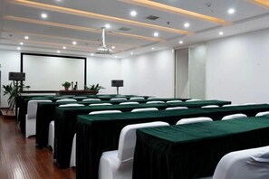 A conference room with rows of tables, white chairs, a projector screen, and a ceiling with recessed lighting. - Yijing International Hotel (Fuyang)