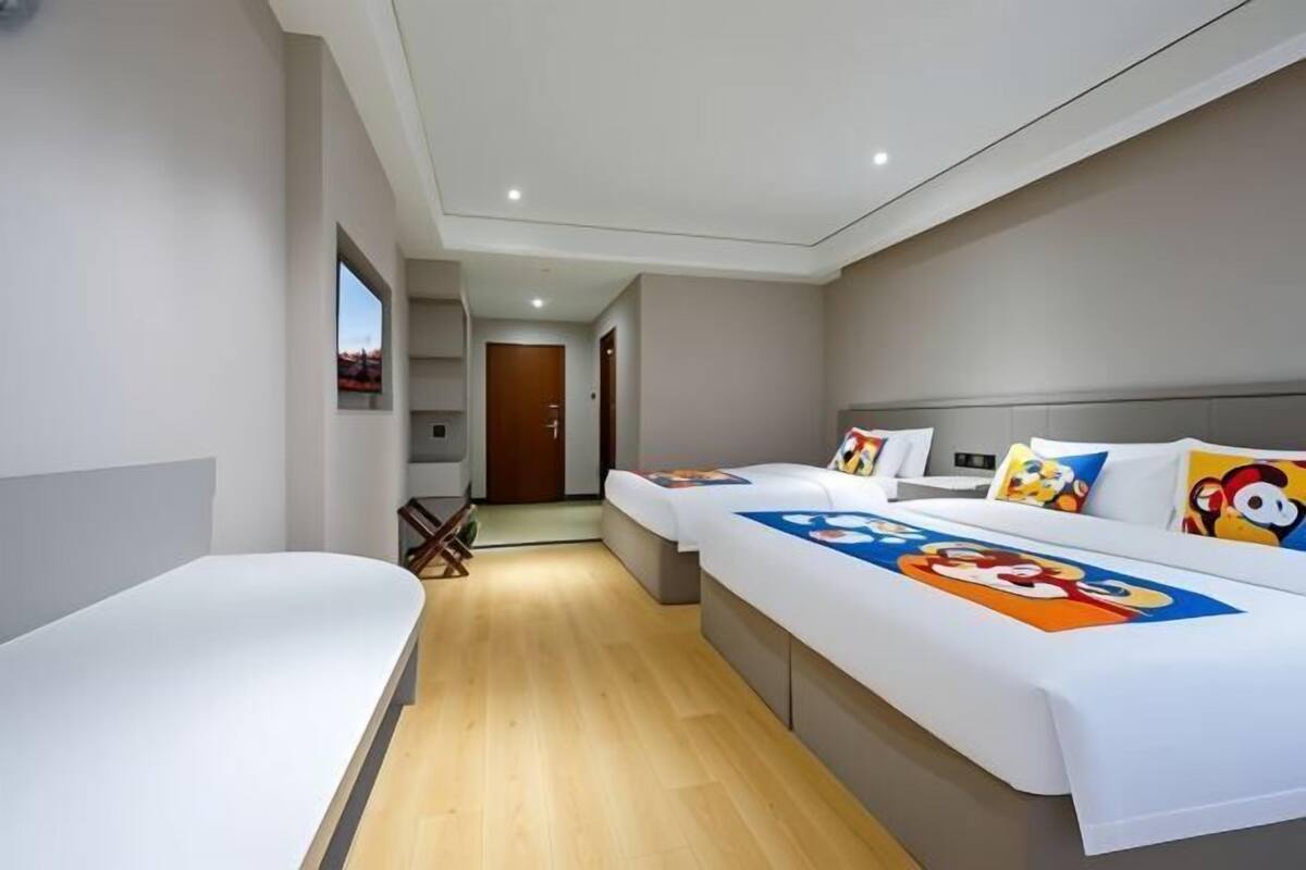 Een moderne hotelkamer met een groot bed, een kleiner bed en een bureau. Er is een raam dat natuurlijk licht biedt en een deur die naar een andere kamer leidt.