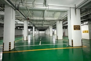 Un estacionamiento de varios niveles con pilares blancos, suelo verde y líneas amarillas que delimitan los espacios de estacionamiento.