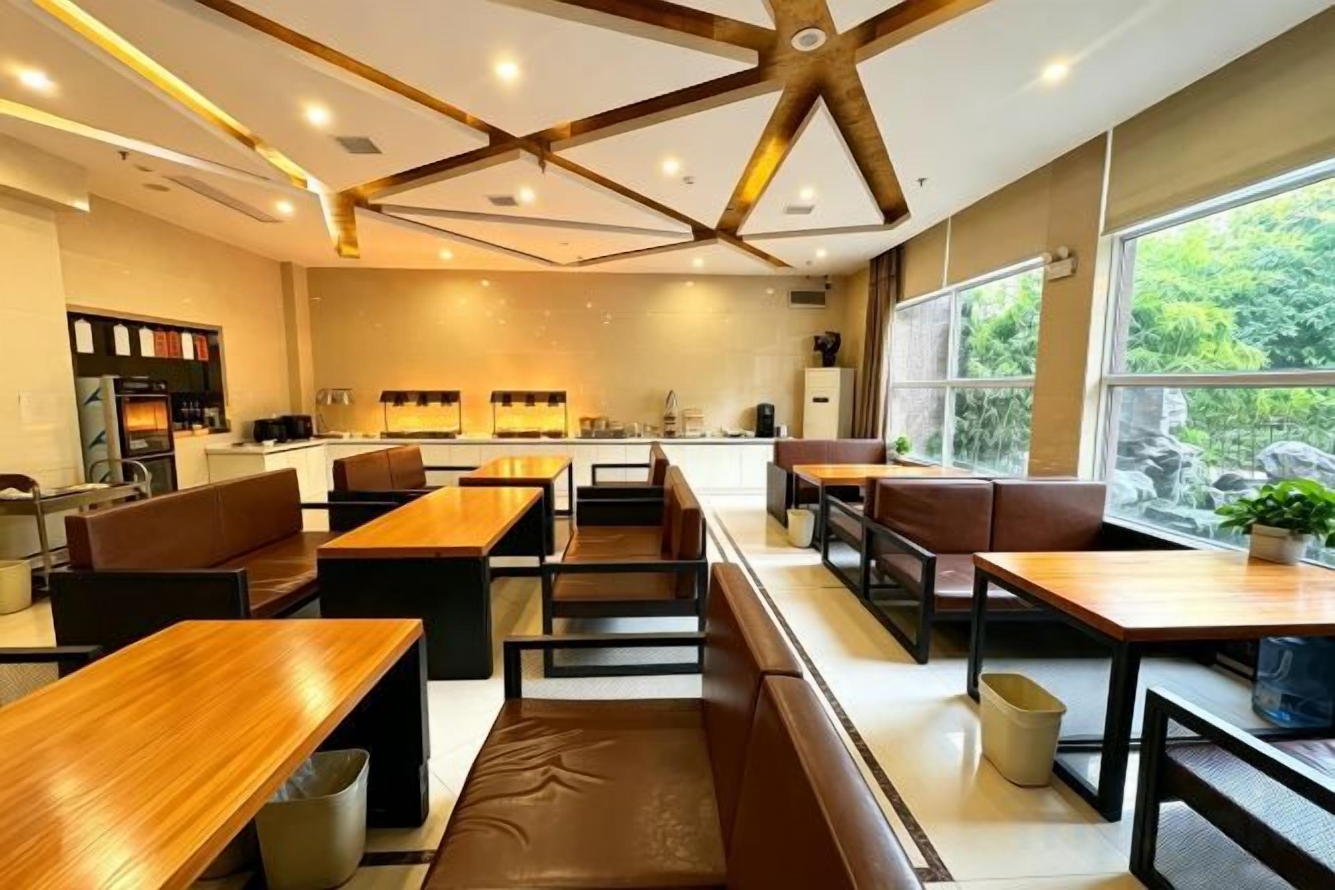 Ein modernes Restaurant mit Holztischen und -sitzen, einem Küchenbereich und großen Fenstern mit Blick ins Freie.