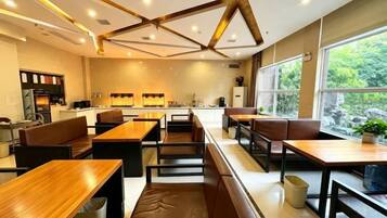 Ein modernes Restaurant mit Holztischen und -sitzen, einem Küchenbereich und großen Fenstern mit Blick ins Freie.