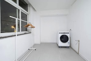 A small, clean laundry room with a washing machine, a drying rack, and a window.