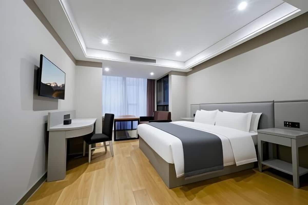 Een moderne hotelkamer met een bed, bureau, stoel en een televisie aan de muur.