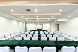 A conference room with rows of white chairs, a long table with a green tablecloth, and a projector screen at the front.