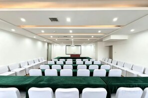 A conference room with rows of white chairs, a long table with a green tablecloth, and a projector screen at the front. - YIJING International Hotel (Fuyang)