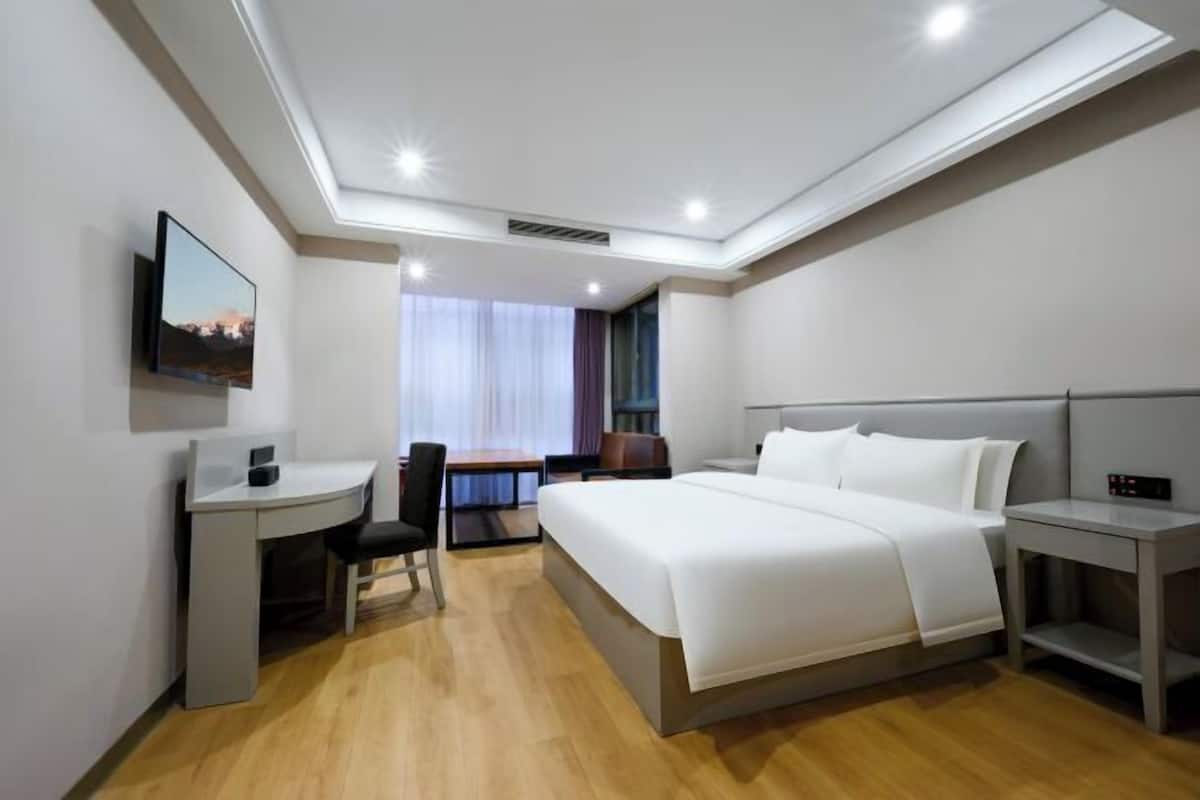 Een hotelkamer met een bed, bureau, stoel en een televisie aan de muur.