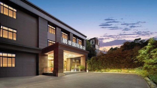 Un hotel con fachada moderna, entrada bien iluminada y zona ajardinada en el frente.