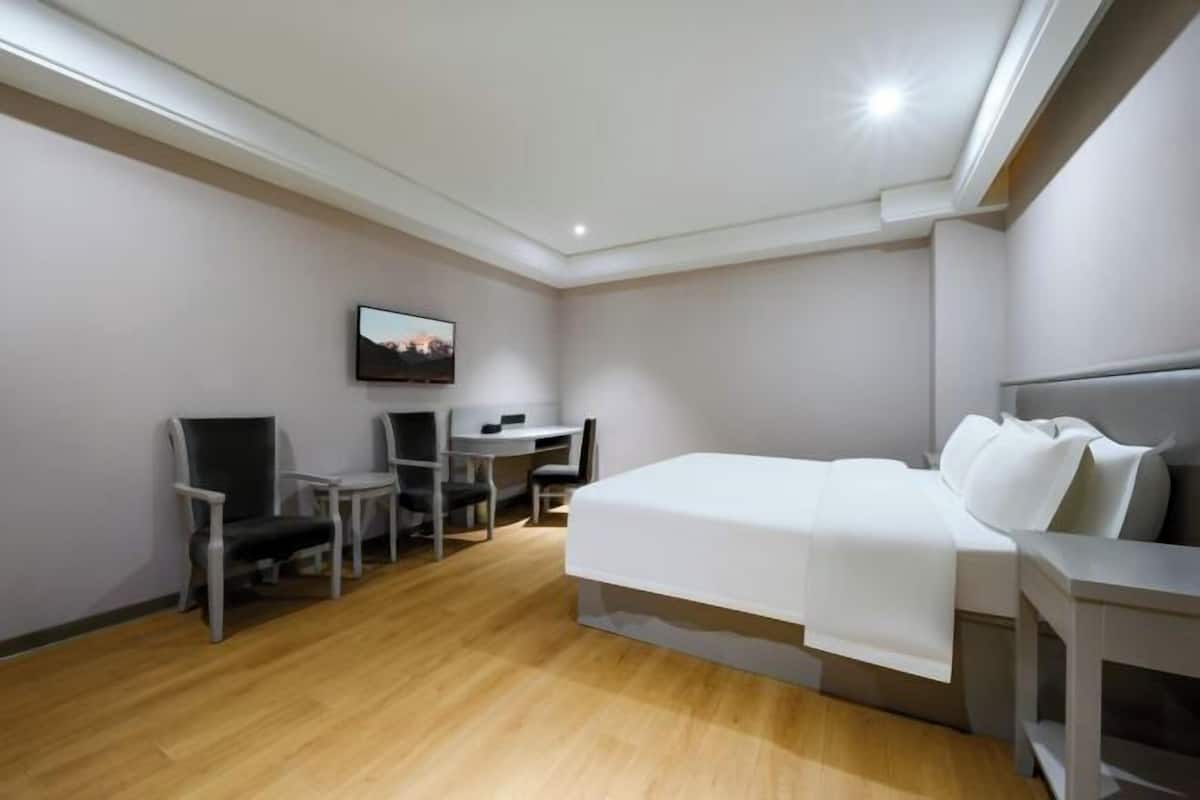 Een hotelkamer met een bed, een bureau, een stoel en een televisie aan de muur.