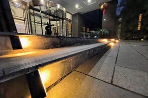 A nighttime outdoor area with a bench and a pathway leading to a building entrance.