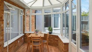 Une véranda avec une table et des chaises en bois, une plante en pot et une vue sur l’extérieur.