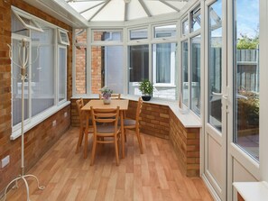 Ein Wintergarten mit Holztisch und -stühlen, einer Topfpflanze und Blick ins Freie.
