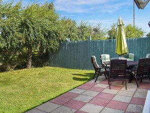 Un patio con mesa y sillas, un paraguas verde y una cerca de madera.