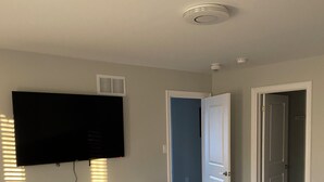 A bedroom with a bed, a dresser, a television, and two doors leading to other rooms.