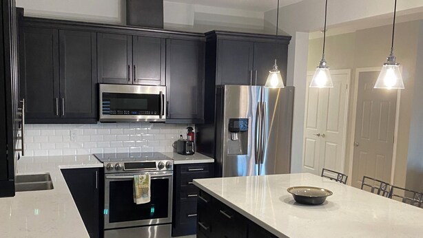 A modern kitchen with dark cabinets, stainless steel appliances, a large island, and pendant lighting.