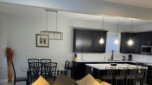 A modern living room with a sectional sofa, a glass coffee table, and a dining area with chairs and a kitchen in the background.
