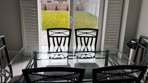 A glass table with two chairs in a room with a sliding glass door leading to a backyard.