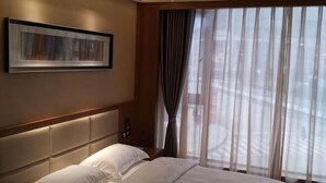 Habitación de hotel con una cama grande, cabecero, teléfono montado en la pared y una ventana con cortinas.