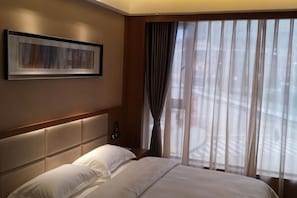 A hotel room with a large bed, a headboard, a wall-mounted phone, and a window with curtains. - Shui'an Waterfront Hotel (Weng'an County)