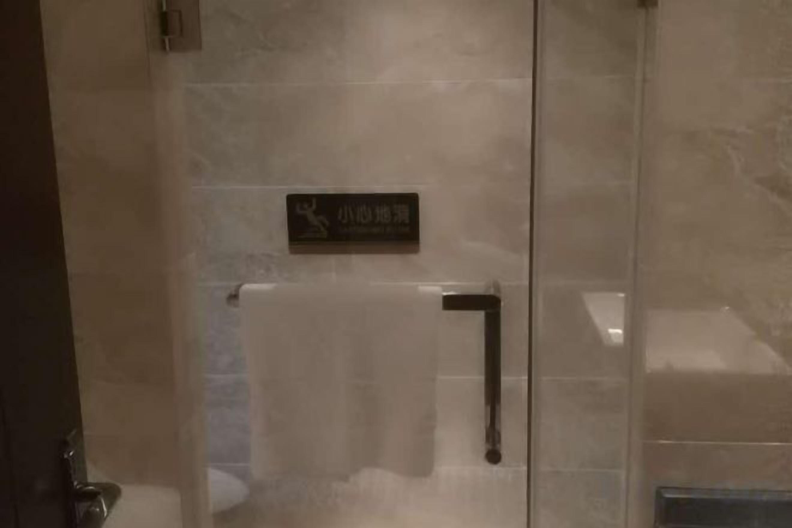 A glass door with a sign, a towel rack, and a shower area.