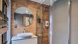 Ein modernes Badezimmer mit einer Glaskabine, einem runden Spiegel und einem weißen Waschtisch.