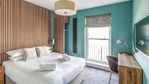 Ein modernes Schlafzimmer mit einem großen Bett, einem Holzkopfende, einem Fenster mit Aussicht, einem Schreibtisch und einem Stuhl.