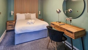 Ein Hotelzimmer mit Bett, Schreibtisch, Stuhl, rundem Spiegel und Wandlampe.