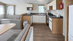 A compact kitchen with a microwave, toaster, sink, and stove. There is a small dining area with a table and bench.