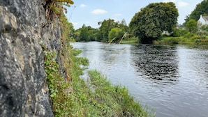 A river with a stone wall on one side and a tree-lined bank.