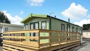 A green mobile home with a wooden deck in front.