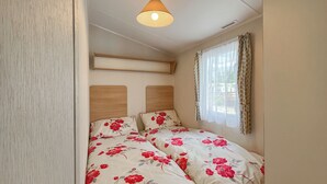 A bedroom with two beds, wooden headboards, a ceiling light, and a window with curtains.