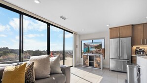 A modern kitchen with a large refrigerator, a dining area, and a view of a mountainous landscape through large windows.