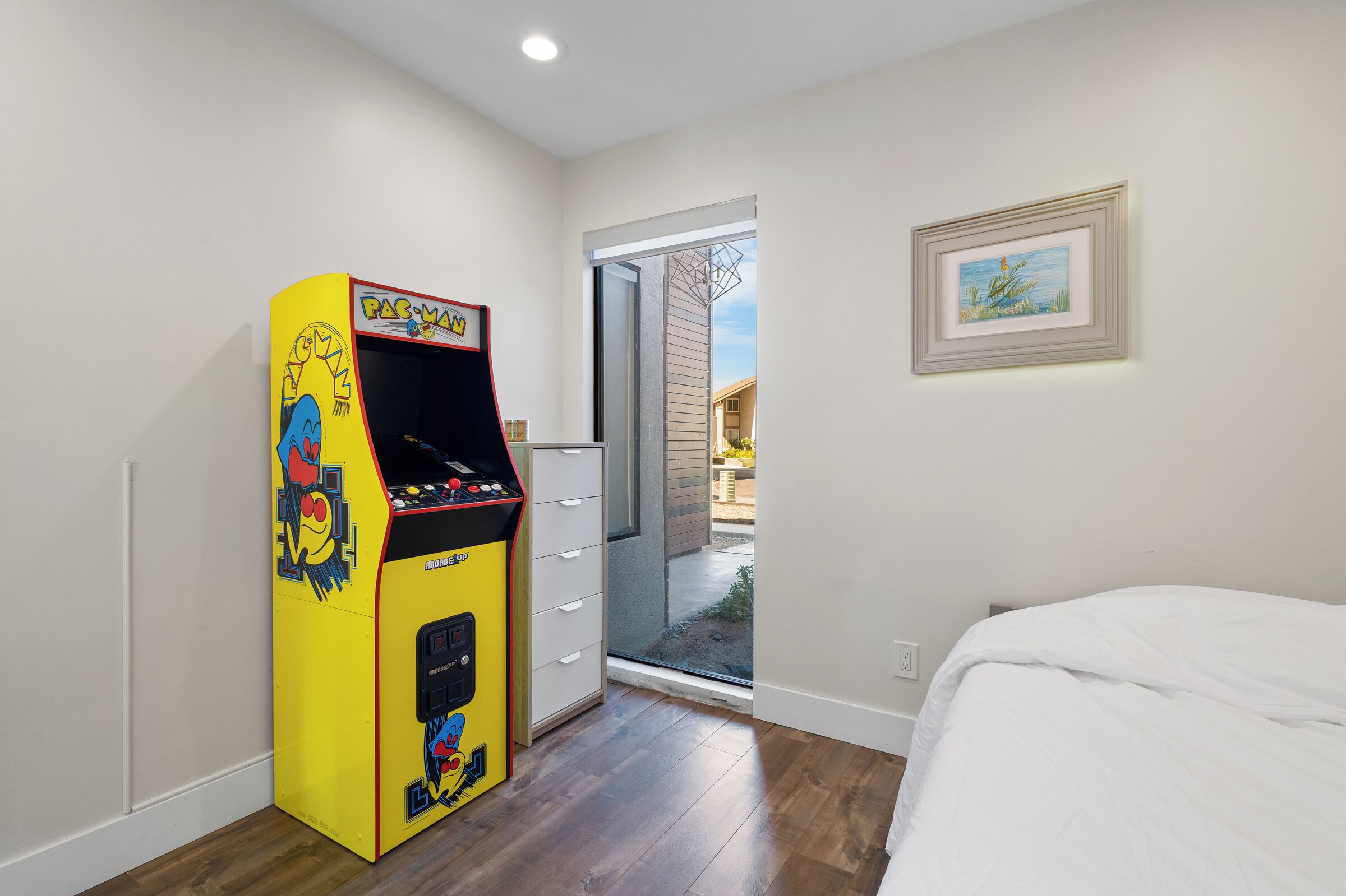 A room with a Pac-Man arcade machine, a bed, and a door leading to an outdoor area.