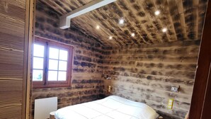 A wooden cabin bedroom with a bed, a small stool, and a window.