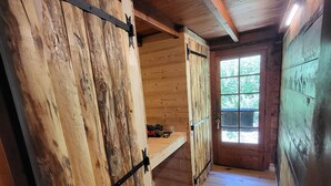 A rustic wooden interior with a loft bed, a window with a view, and a wooden floor.