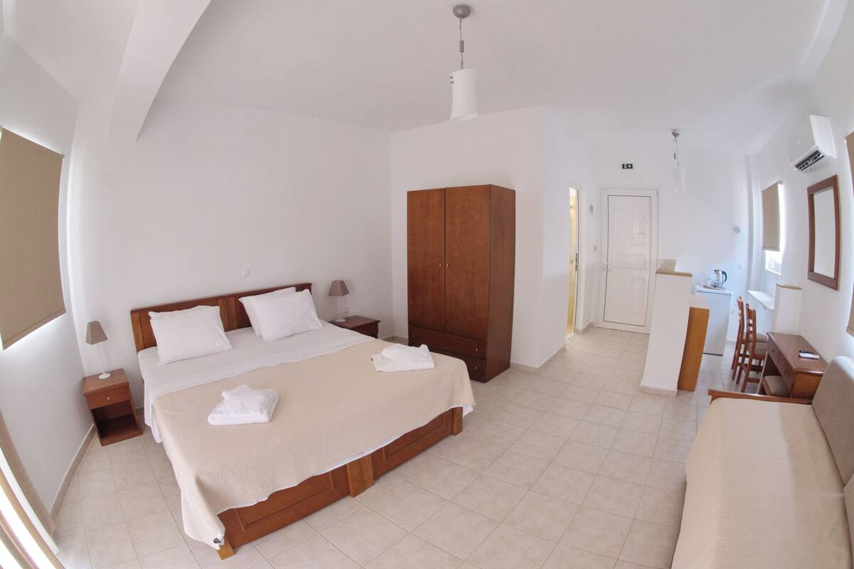 A bedroom with a large bed, a wardrobe, a desk, and a chair.