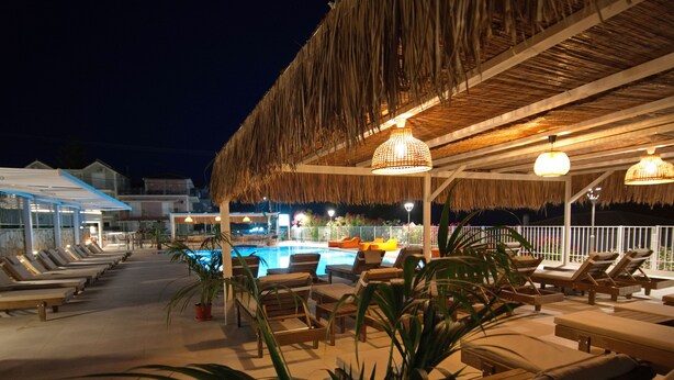 Un espace aménagé au bord de la piscine, avec des chaises longues et une structure dotée d’un toit de chaume.