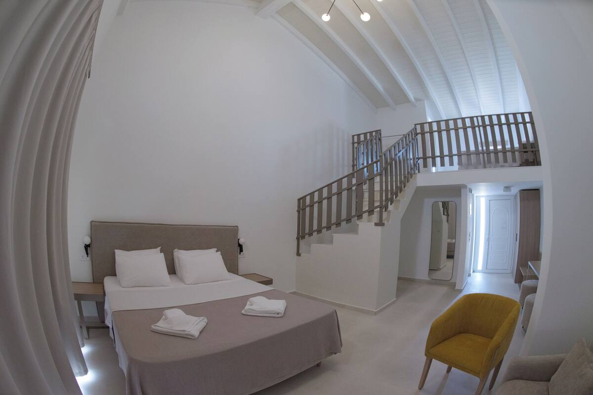 A spacious bedroom with a large bed, a staircase leading to an upper level, and a bright, modern design.