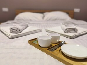 A neatly made bed with pillows and a tray with two cups, a spoon, and a plate. - HAYQ BOUTIQUE HOTEL (Yerevan)