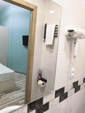A hotel bathroom with a mirror, a towel rack, a hairdryer, a bottle of hand soap, and a toilet paper holder. - HAYQ BOUTIQUE HOTEL (Yerevan)