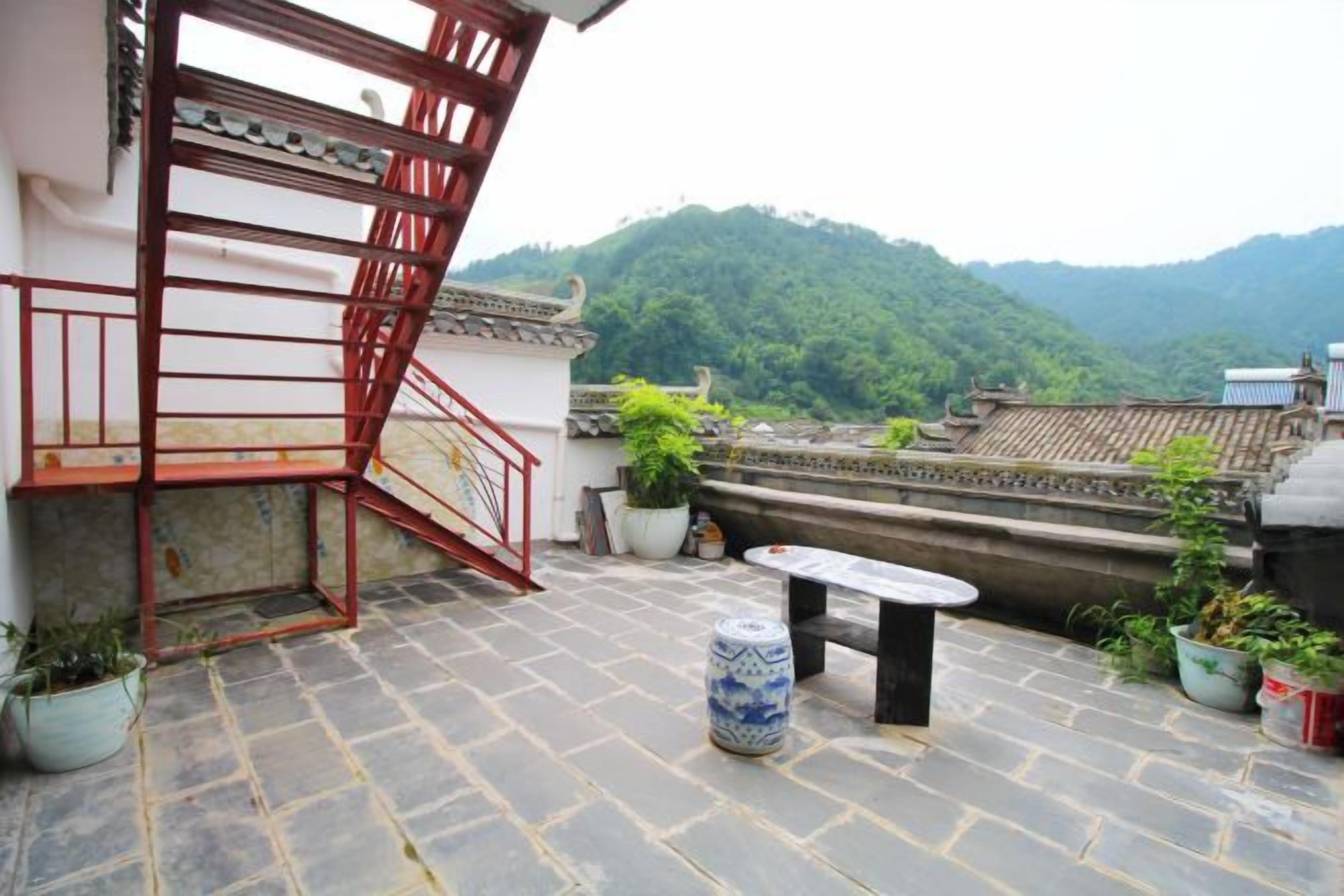 A rooftop terrace with a red metal staircase, potted plants, and a stone floor.